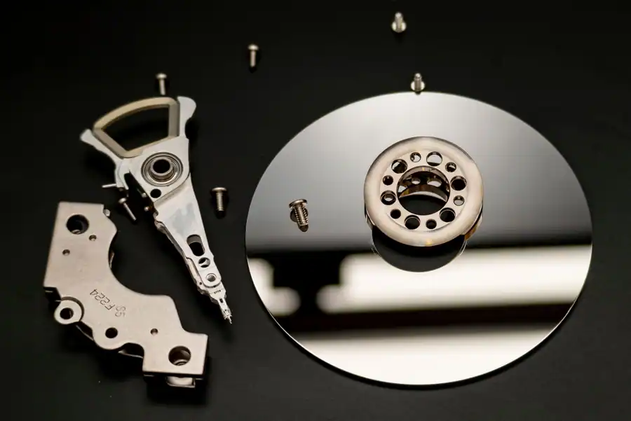 Close-up of dismantled hard drive parts with a reflection on a black surface, showcasing intricate mechanical details.